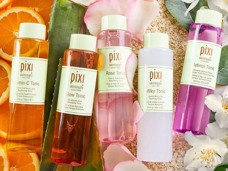 Her ses fem Pixi Beauty produkter i lyserøde og orange nuancer. De ligger på forskellige planter.