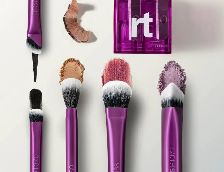 Her ses fem lilla makeupbørster fra Real Techniques på en lysegrå baggrund.