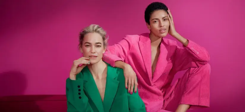 Her ses en pink baggrund. Der er to kvinder i jakkesæt - det ene er grønt og det andet er pink.