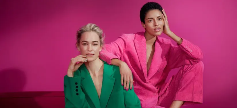 Her ses en pink baggrund. Der er to kvinder i jakkesæt - det ene er grønt og det andet er pink.