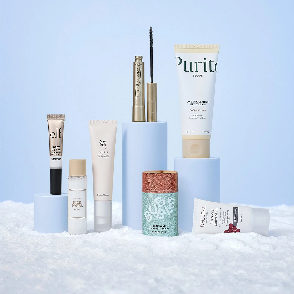 Syv hudpleje- og makeup-produkter, inkl. elf concealer, L'Oreal mascara og Purito creme, præsenteret i et snelandskab.
