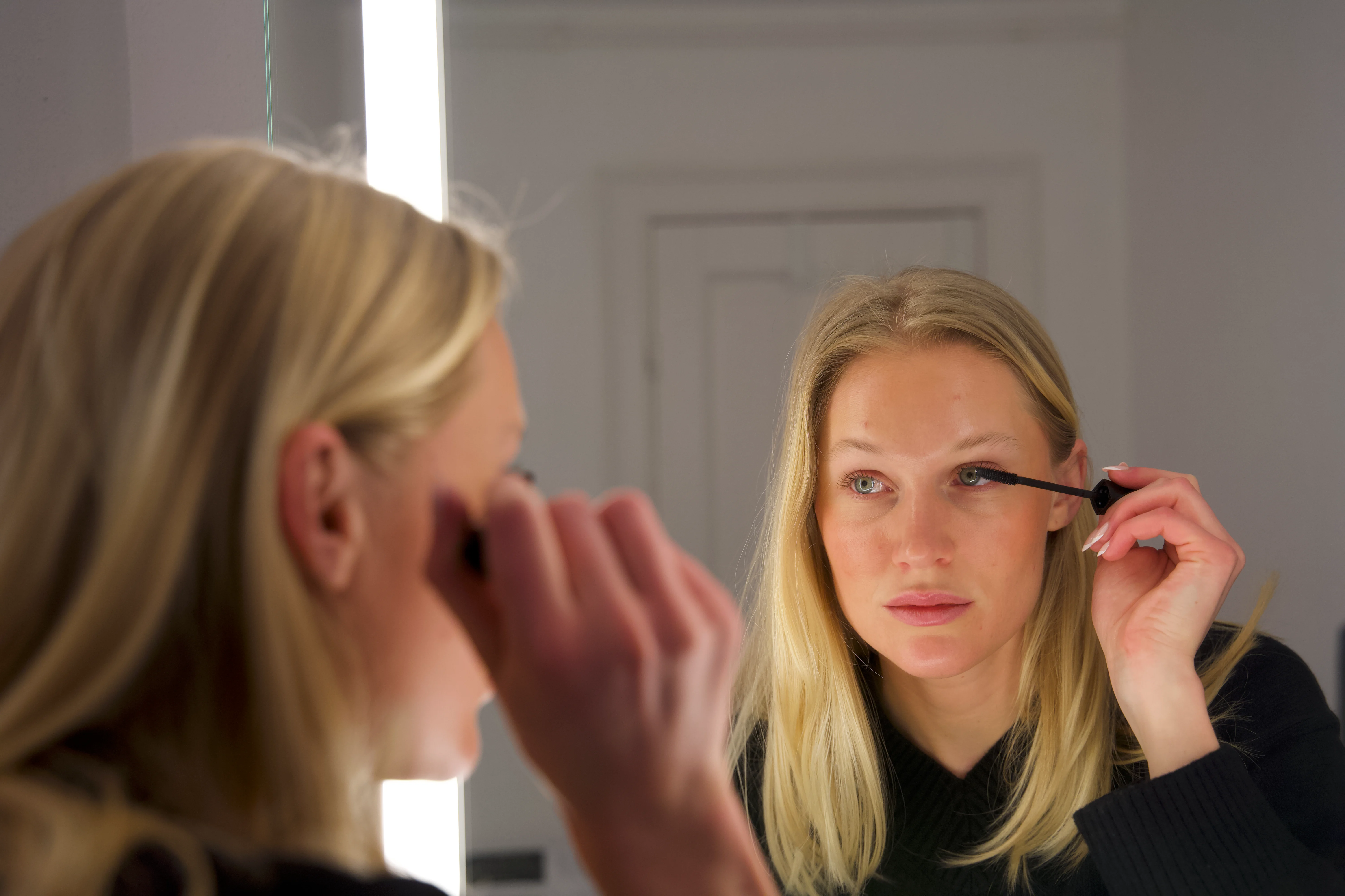 Kvinde, der lægger mascara i spejlet