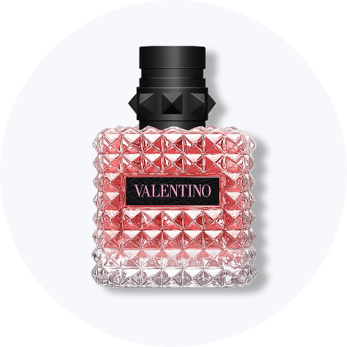 Her ses et billede af en parfumeflakon fra Valentino placeret centralt mod en lys, rund baggrund. På flakonen står teksten “VALENTINO”. Flakonen er i pink og transparente nuancer med sort låg og nitteinspireret mønster.