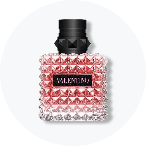Her ses et billede af en parfumeflakon fra Valentino placeret centralt mod en lys, rund baggrund. På flakonen står teksten “VALENTINO”. Flakonen er i pink og transparente nuancer med sort låg og nitteinspireret mønster.
