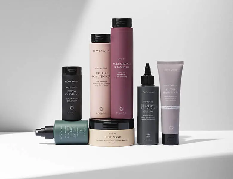 Her ses et billede med flere hårplejeprodukter fra Løwengrip placeret samlet på en lys overflade mod en lys baggrund. På produkterne står blandt andet “Volumizing Shampoo”, “Color Conditioner”, “Detox Shampoo”, “Hair Mask” og “Sensitive Dry Scalp Serum”. Produkterne er i forskellige farver som beige, rosa, sort og grøn.