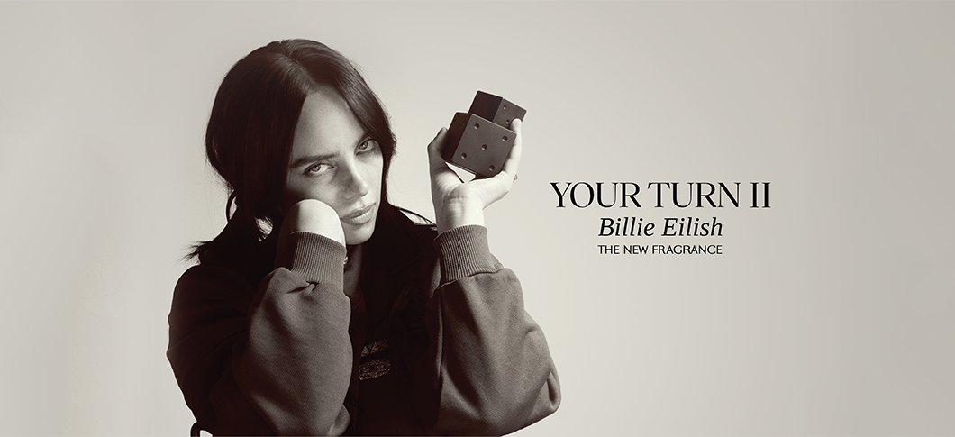 Her ses et billede med en person til venstre, der holder en parfumeflakon, mod en lys baggrund. Til højre står teksten “YOUR TURN II Billie Eilish” samt “THE NEW FRAGRANCE”.