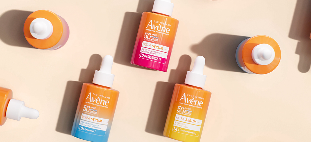 Her ses Avène Ultra Serum produkter i orange, pink og blå emballage på en lys beige baggrund.