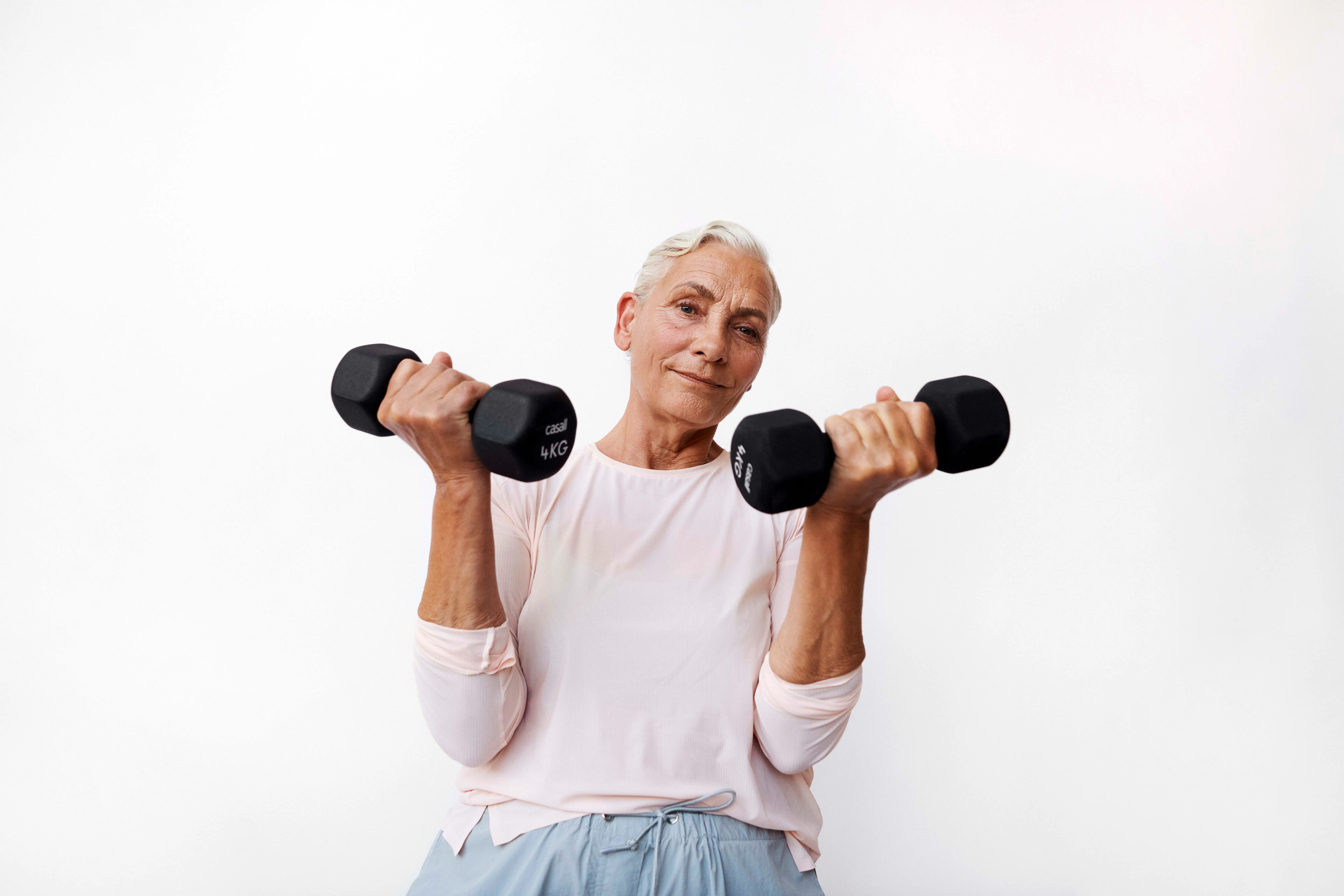 En ældre person løfter to sorte Casall 4KG håndvægte og kigger mod kameraet.