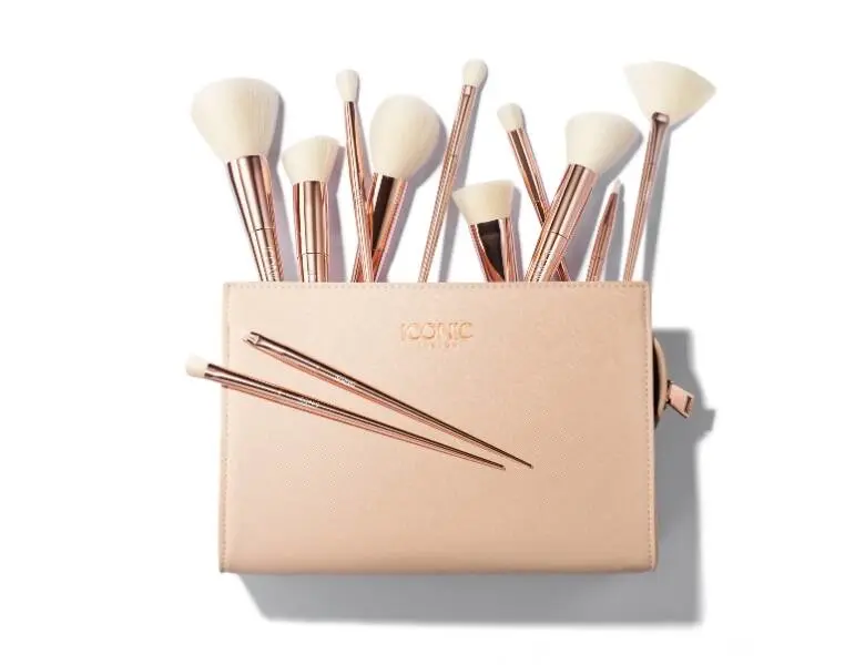 Her ses en hvid baggrund med en lyserød makeuptaske. Den er fyldt med makeupbørster. 