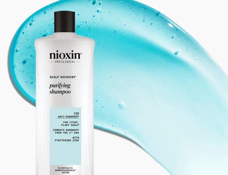 Her ses et billede af en shampoo fra Nioxin placeret mod en lys baggrund med blå gelstruktur bagved. På flasken står teksten “nioxin PRO CLINICAL SCALP RECOVERY purifying shampoo”. Produktet er udviklet til skæl og tør, irriteret hovedbund.