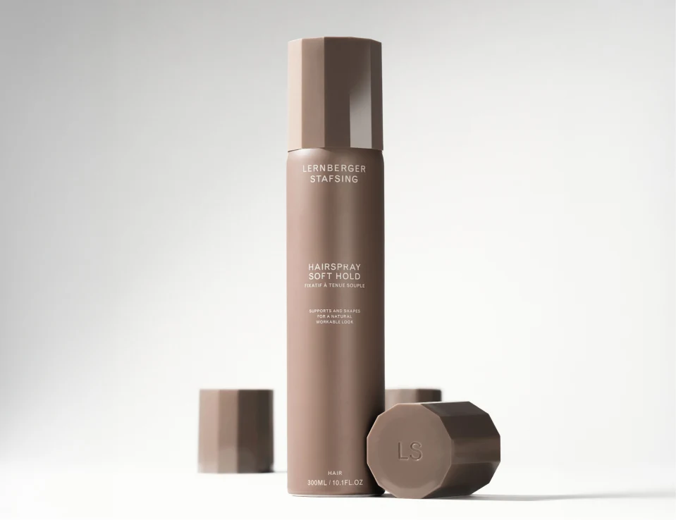 Her ses Lernberger Stafsing Hairspray Soft Hold i en høj brun sprayflaske. Ved siden af står et låg og en brun, facetteret beholder med LS på toppen.