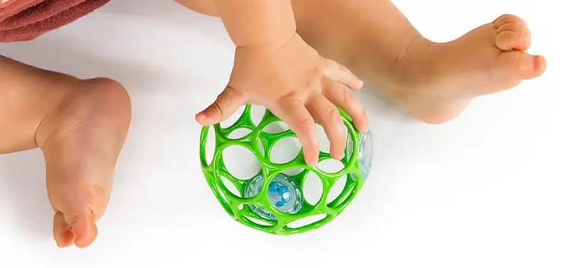 Baby sidder på lyst underlag og holder en grøn hul bold mellem hænder og fødder.
