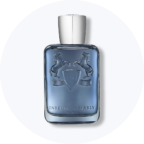 Her ses et billede af en parfumeflakon fra Parfums de Marly placeret centralt mod en lys, rund baggrund. Flakonen er i blå nuance med sølvfarvet låg og relieflogo med to heste på fronten.
