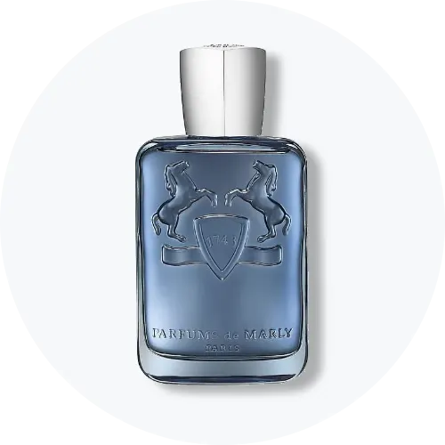 Her ses et billede af en parfumeflakon fra Parfums de Marly placeret centralt mod en lys, rund baggrund. Flakonen er i blå nuance med sølvfarvet låg og relieflogo med to heste på fronten.