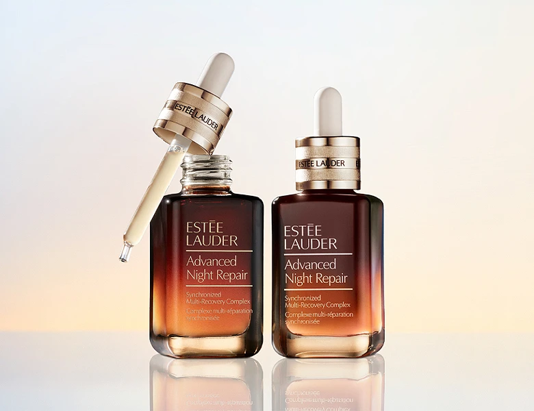 Her ses et billede med serumprodukter fra Estée Lauder placeret mod en lys baggrund. På flaskerne står teksten “Advanced Night Repair”, og det ene produkt vises med pipette.