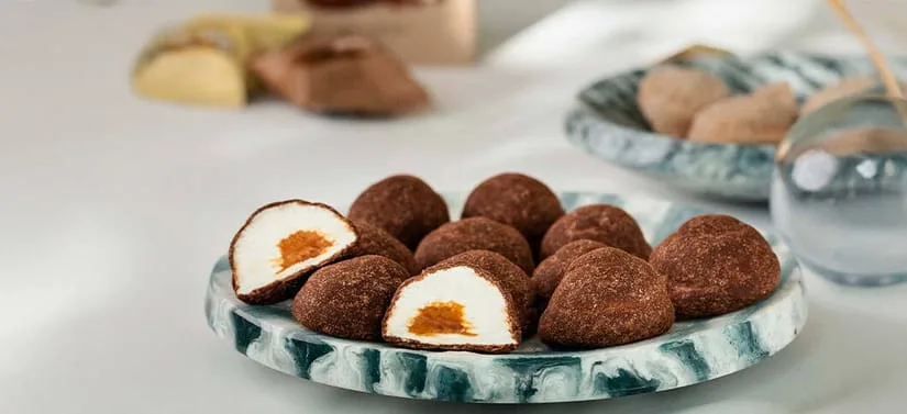 Et fad mørkeblå og lyseblå nuancer fyldt The Mallows caramelfyldte skumfiduser i brun. En er skåret over, så man kan se indeni, hvor der er fyldt med karamel i den hvide skumfidus.