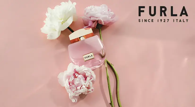 Her ses en Furla parfume blandt blomster på en lyserød baggrund.