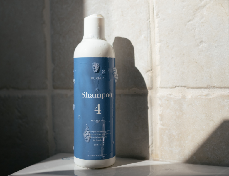 Her ses et billede af et hårplejeprodukt fra Purely Professional placeret mod en lys flisebaggrund. På flasken står teksten “Shampoo 4”, og produktet er i hvid og blå emballage.
