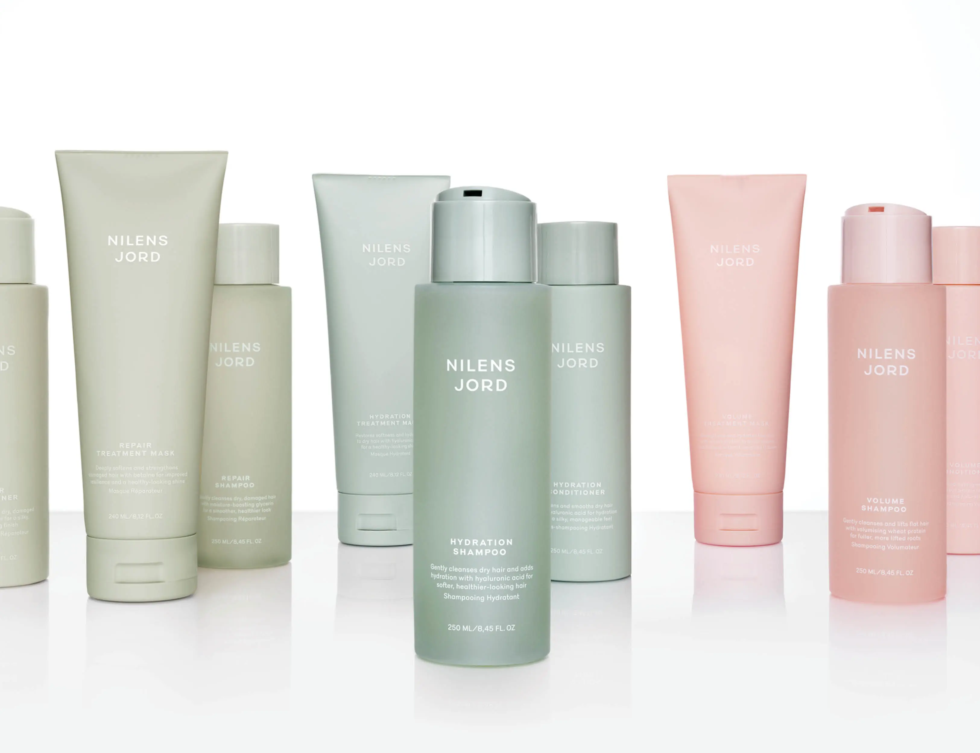 Her ses et billede med flere hårplejeprodukter fra Nilens Jord placeret mod en lys baggrund. Produkterne omfatter blandt andet shampoo, conditioner og hårmasker i grønne og lyserøde nuancer.