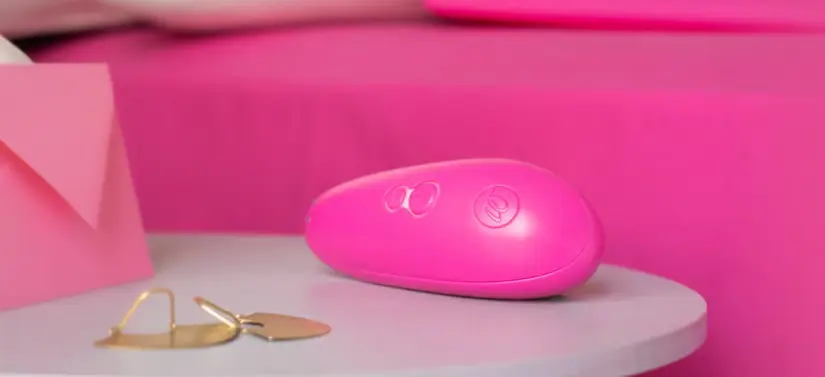Her ses et billede af et pink produkt, som ligger på et lyst bord. I baggrunden ses en pink seng.