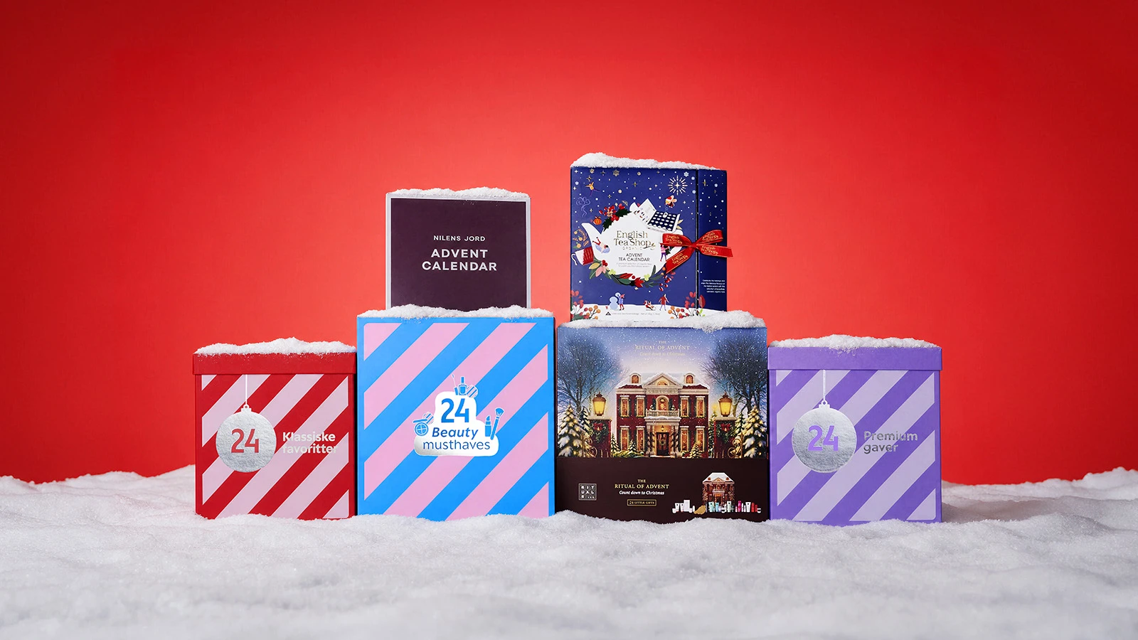 Seks julekalendere dækket med sne: Nilens Jord, English Tea Shop, 24 Klassiske favoritter, 24 Beauty musthaves, The Ritual of Advent og 24 Premium gaver. Rød baggrund.