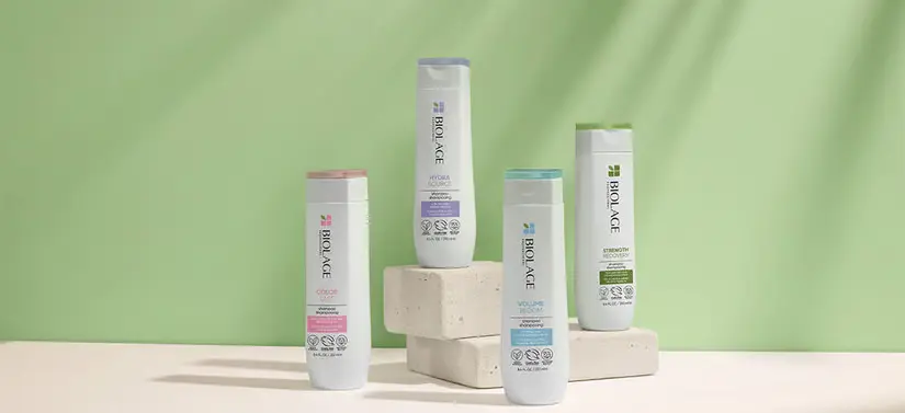 Her ses en grøn baggrund med fire Biolage produkter i hvid med henholdsvis lyserøde, lilla, blå og grønne detaljer. 