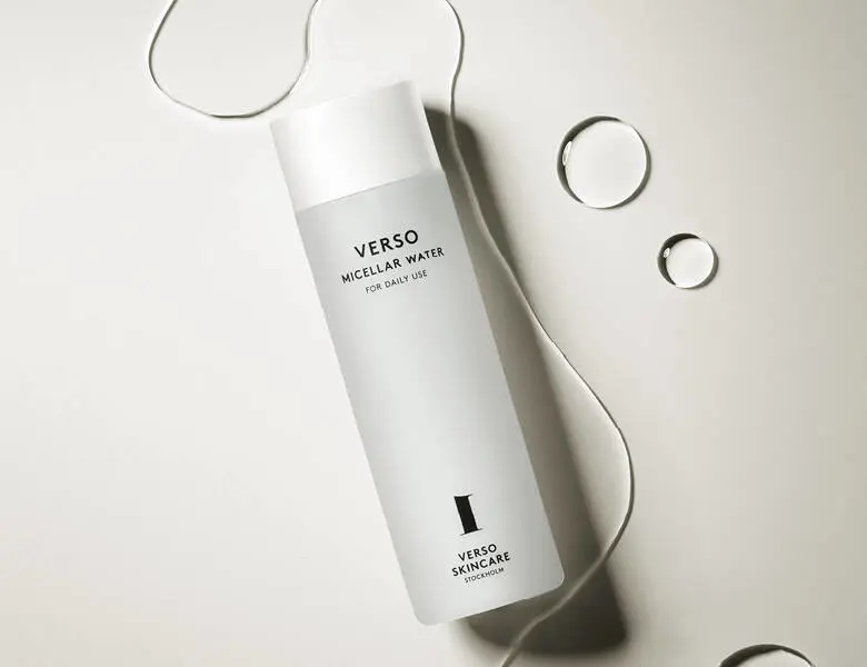 Her ses et Verso produkt med noget klart væske omkring sig. Baggrunden er en lys beige-grå farve.