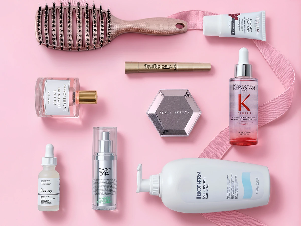 Et udvalg af skønhedsprodukter: Kérastase serum, The Ordinary, Zarkoperfume, Fenty Beauty og Biotherm kropslotion på lyserød baggrund.