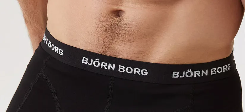 Her ses et close-up billede af en mands mave. Han har sorte underbukser på.