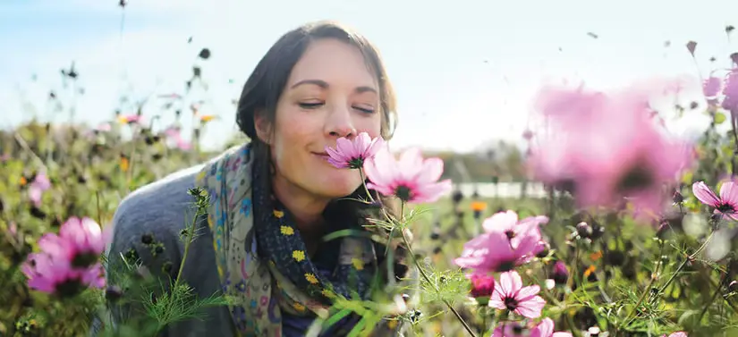 Her ses en kvinde ude på en blomstermark. Hun dufter til en lyserød blomst.