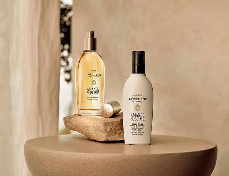 Her ses L’Occitane kropsplejeprodukter i flasker på et beige bord i et lyst miljø.
