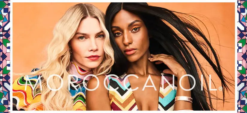 Her ses en orange baggrund med to kvinder - en med lyst og en med mørkt hår. Foran dem ses MoroccanOil-logoet i hvid. 