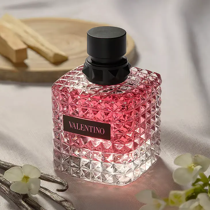 Valentino parfume i en lyserød, firkantet, tekstureret glasflaske med sort låg. Tekst: VALENTINO. Med vanilje og blomster.