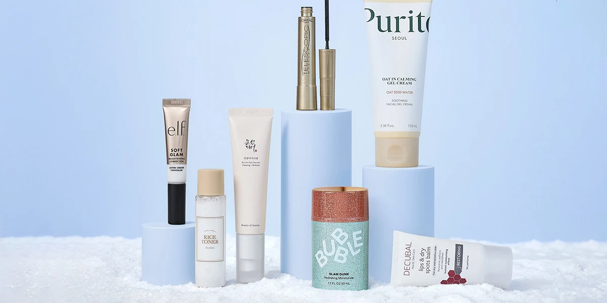 Diverse hudpleje- og makeup-produkter som mascara, cremer og serum, vist på lyseblå podier i sne.