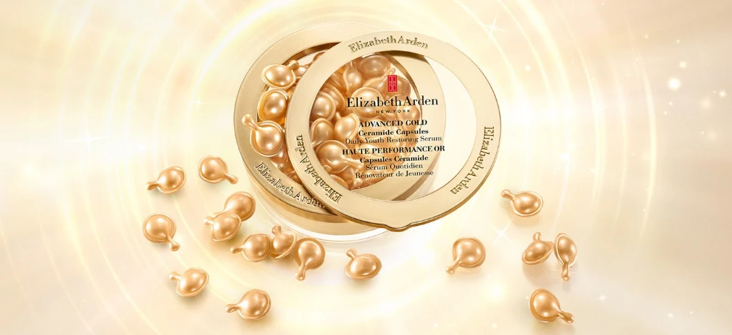 Her ses Elizabeth Arden Advanced Ceramide Gold Daily Youth Restoring Serum-kapsler i en gylden beholder omgivet af gyldne kapsler på en lys gylden baggrund med cirkelformede lyseffekter og små glimt.