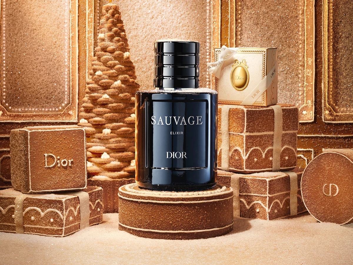 Dior Sauvage Elixir parfume flaske omgivet af festlige honningkagedekorationer, herunder 'Dior' logo kager.