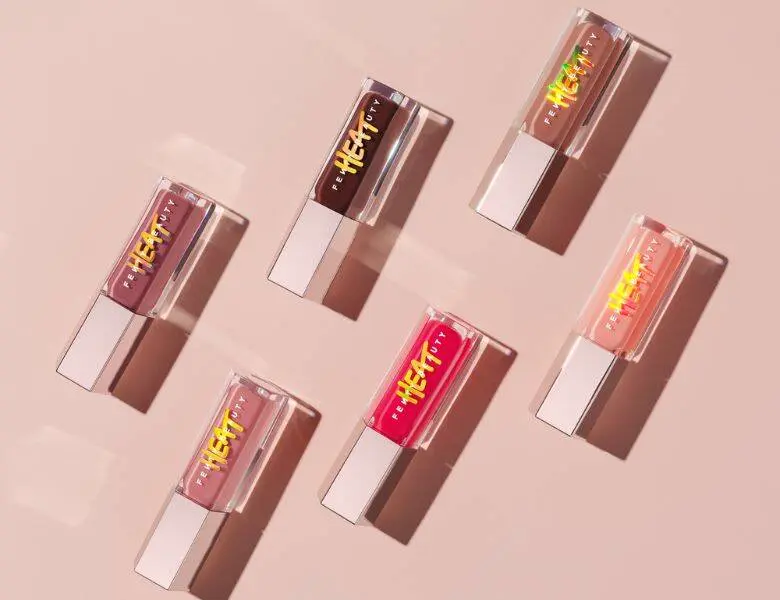 Her ses en beige baggrund med forskellige Fenty Heat lipglosser.