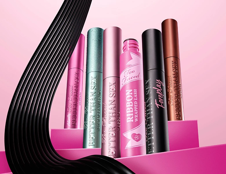 Her ses et billede med flere mascaraprodukter fra Too Faced placeret mod en pink baggrund. På produkterne står blandt andet “Better Than Sex” og “Ribbon Wrapped Lash”.
