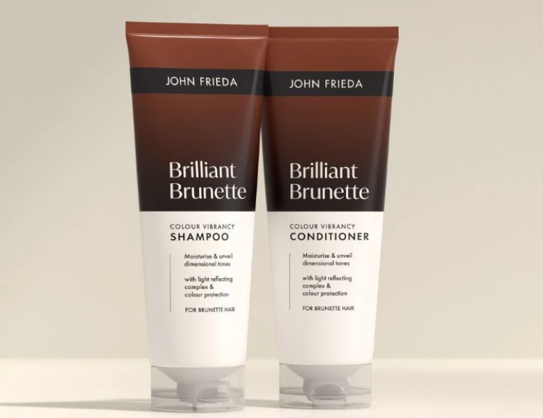 Her ses et billede med hårplejeprodukter fra John Frieda placeret mod en lys baggrund. På produkterne står teksten “Go Blonder”, og serien indeholder shampoo, conditioner og spray. Nederst står teksten “COLOUR”.