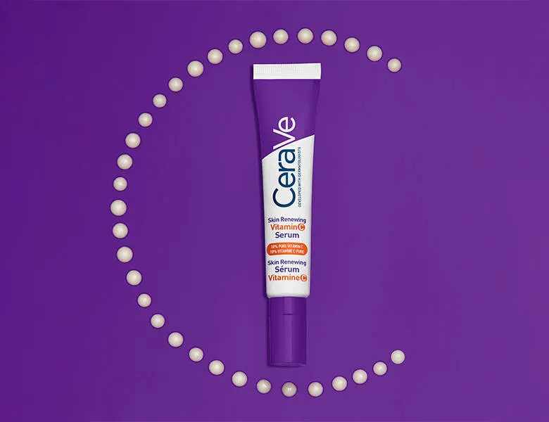 En lilla tube fra CeraVe med teksten “Vitamin C Serum” ligger centreret på en ensfarvet, lilla baggrund. Rundt om tuben er små, ensartede dråber af serum arrangeret i en cirkelform, der danner en dekorativ ramme. Udtrykket er grafisk og farvemættet.