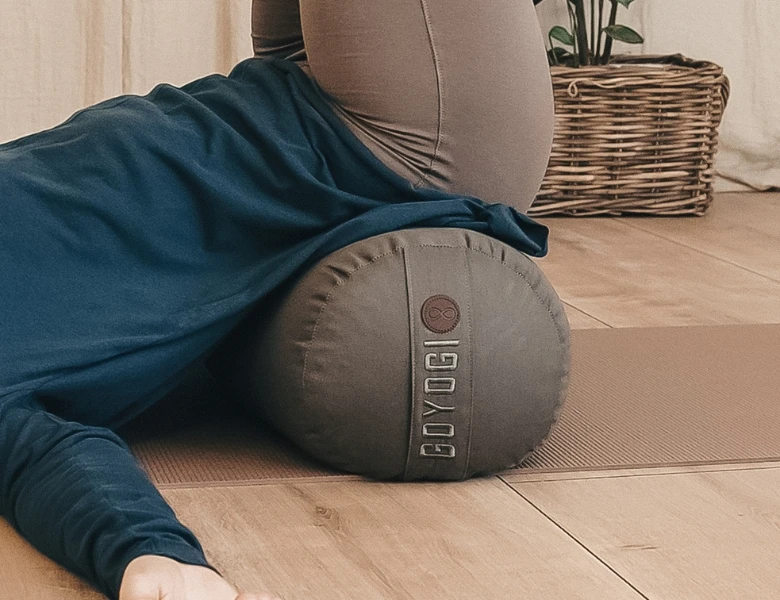 Person ligger på en yogapølle på en måtte i et roligt hjemmemiljø med kurv og plante i baggrunden.