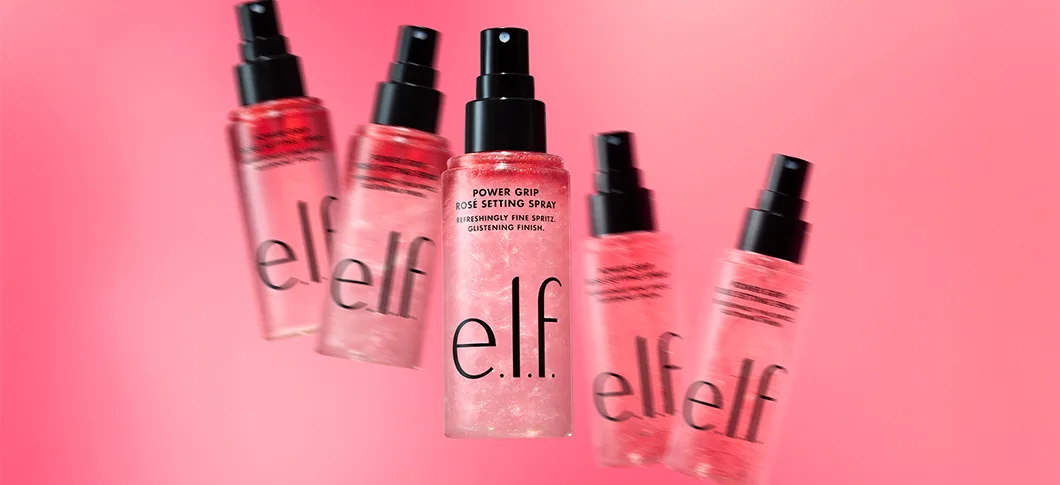 Her ses et billede med flere setting sprays fra e.l.f. placeret mod en pink baggrund. I midten ses produktet “Power Grip Rosé Setting Spray”, mens flere flasker vises omkring det. Produkterne er i pink nuancer med sorte spraytoppe og e.l.f.-logo på fronten.