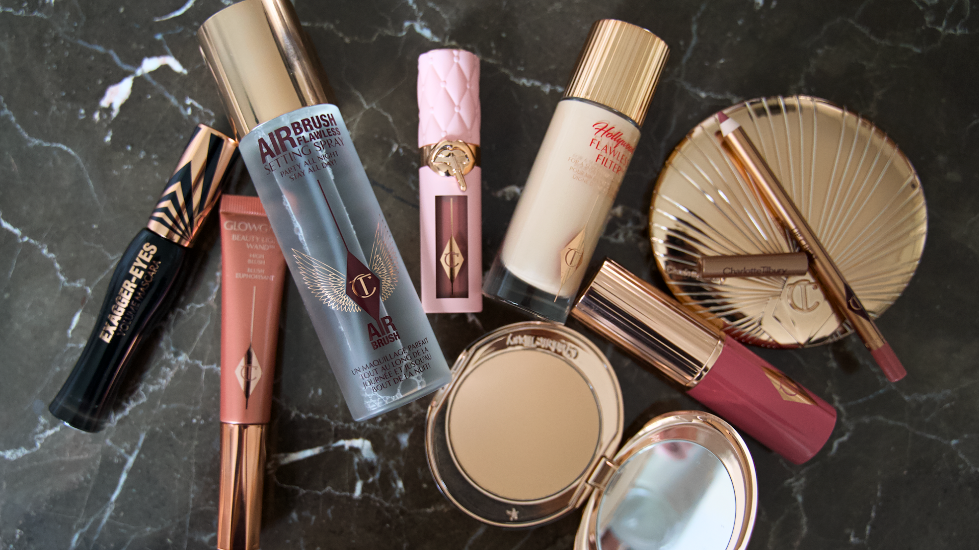 Charlotte Tilbury makeupkollektion: mascara, settingspray, foundation, læbestift og pudderkompakt på marmor.