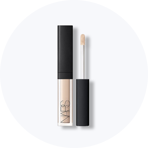 Her ses et billede af et mini makeup-produkt fra NARS placeret centralt mod en lys, rund baggrund. Produktet vises både lukket og åbent med applikator, og emballagen er i lyse nuancer med sort låg og “NARS”-logo på fronten.