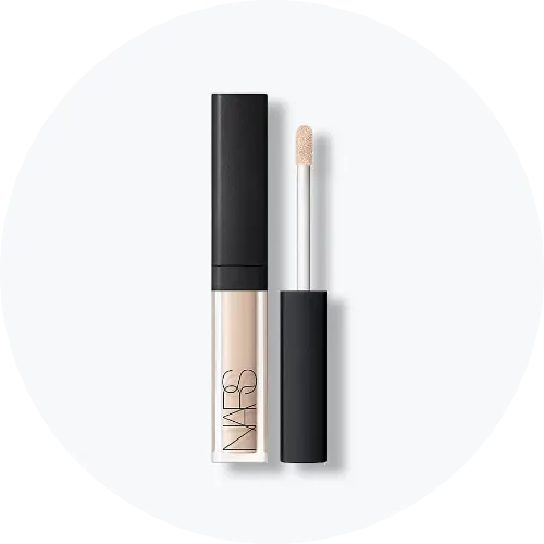 Her ses et billede af et mini makeup-produkt fra NARS placeret centralt mod en lys, rund baggrund. Produktet vises både lukket og åbent med applikator, og emballagen er i lyse nuancer med sort låg og “NARS”-logo på fronten.
