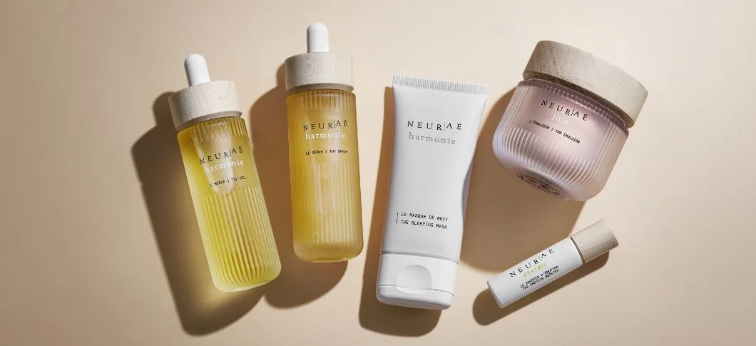 Her ses NEURAÉ hudplejeprodukter – serum, ansigtscreme og maske i lys emballage på en beige baggrund.