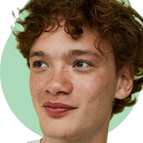 Her ses et ansigt med fregner og krøllet hår foran en lysegrøn baggrund.