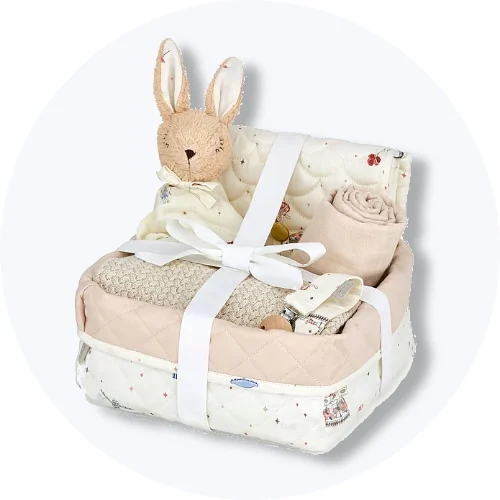 Baby shower gaveæske med bløde babyartikler og kaninbamse i quiltet kurv på lys grå baggrund.
