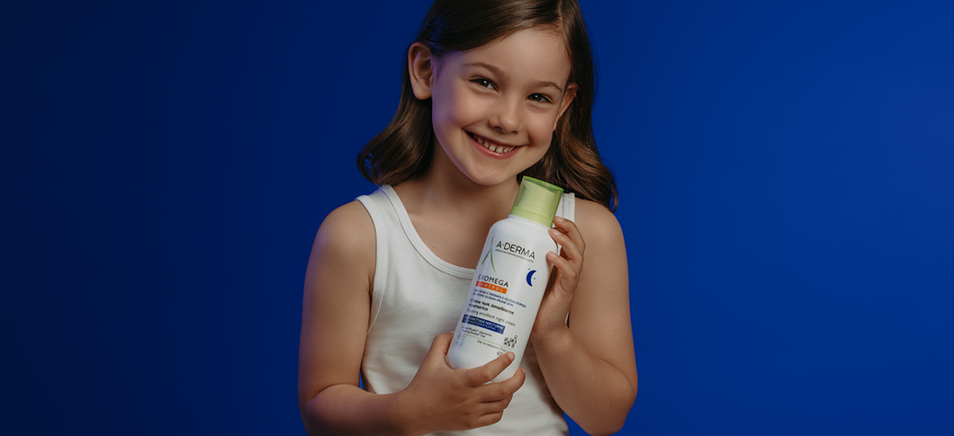 Her ses et barn, der holder en A-DERMA hudplejeflaske på en mørkeblå baggrund.