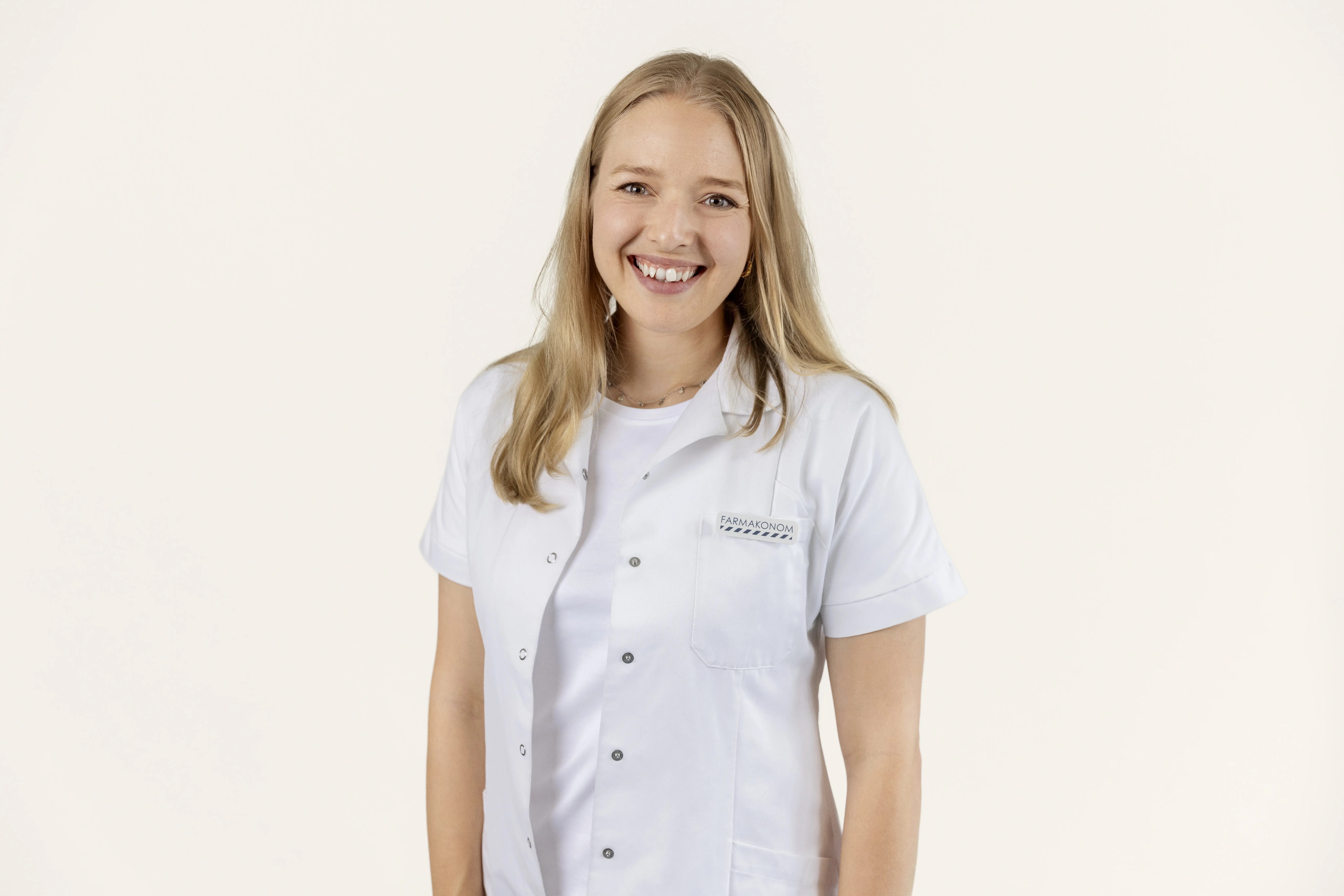 Her ses en smilende farmakonom i hvid kittel på en lys baggrund med teksten “Solpleje til dig med sensitiv hud”